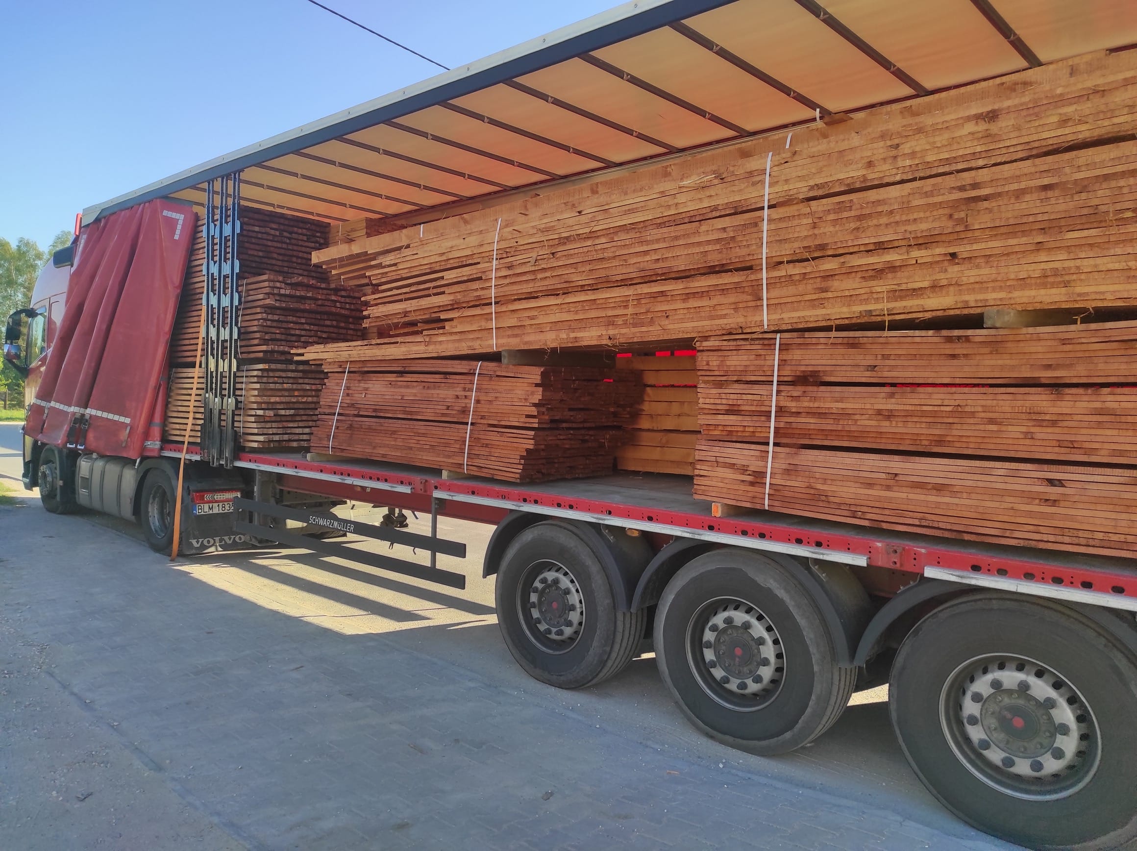 Drewno konnstrukcyje lite 'Ciepło Drewna' na naczepie. Na zdjęciu widać więźbę dachową. Łaty, kontrłaty, stemple budowlane, płyty OSB, kantówki, legary, murłaty, podbitki, deski, krokwie, belki.